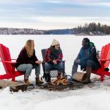 In einer Schneelandschaft am Falcon Lake in Manitoba sitzen drei junge Menschen am Lagerfeuer.