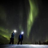 Zwei Wanderer schauen bei Nacht gen Himmel, an dem Polarlichter zu sehen sind